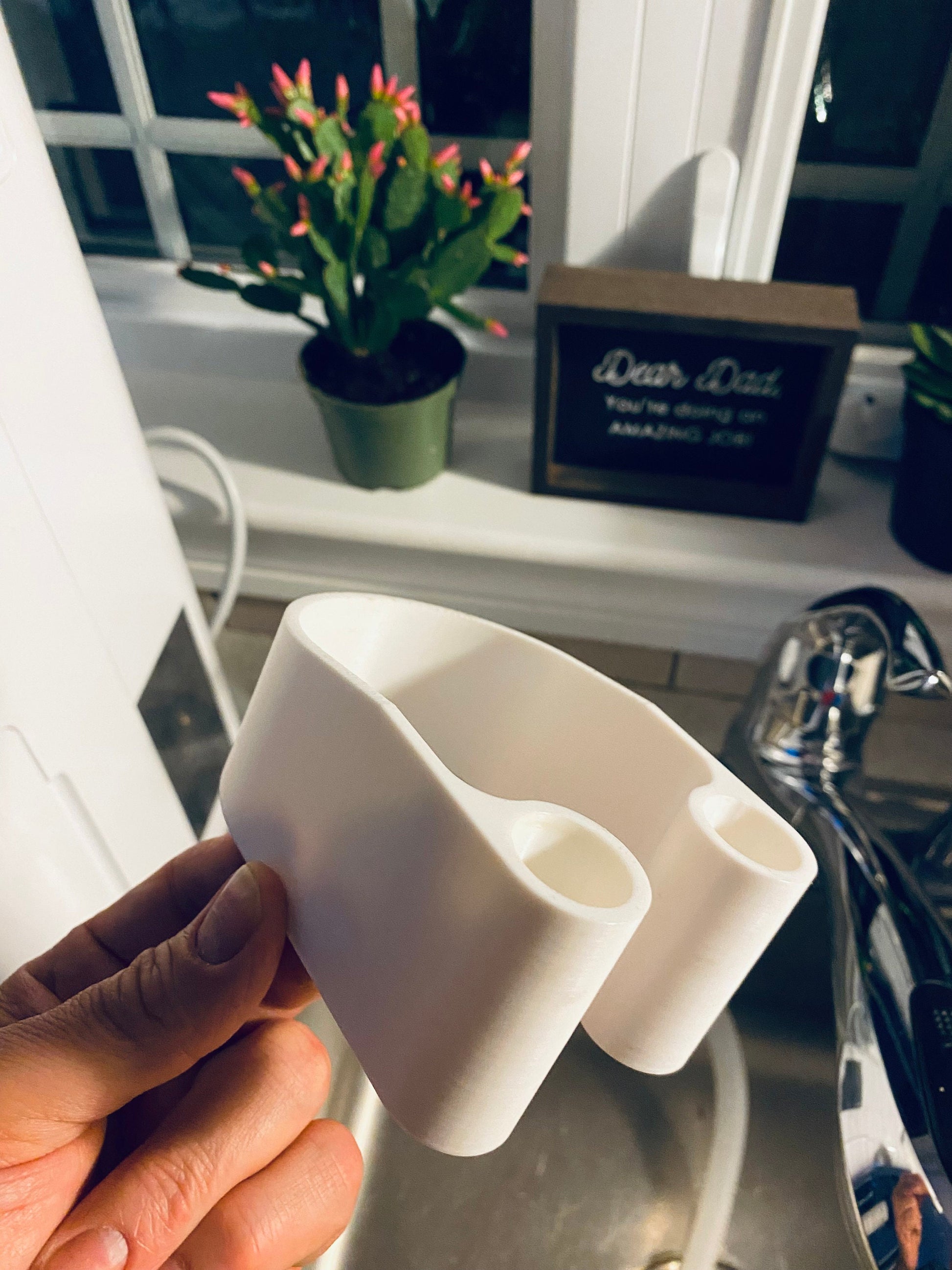 Hand holding 3D printed dehumidifier drain hose bracket showing shape and design
