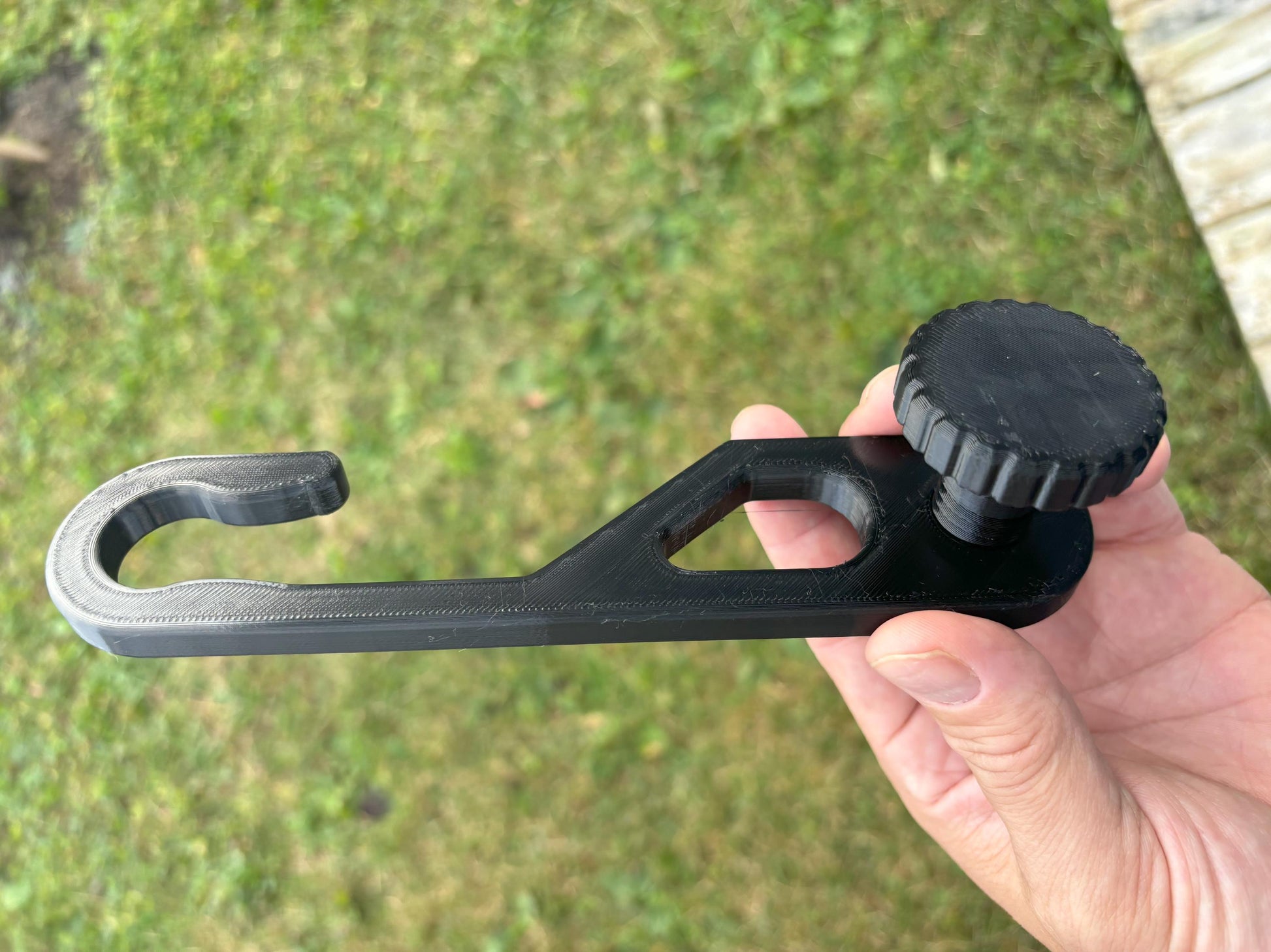 Standard-hook black shower caddy extension hanger displayed with outdoor lighting held in hand for size reference.