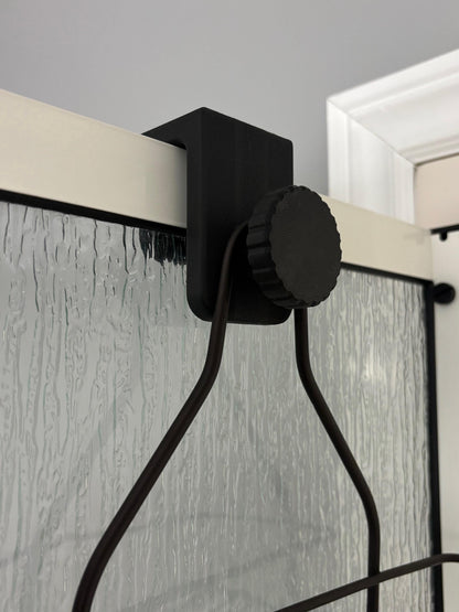 Shower caddy glass wall adapter block in black shown in use on a glass shower partition