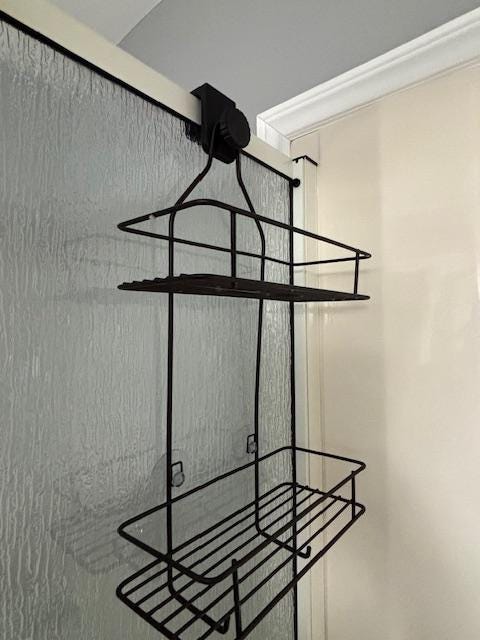Black shower caddy adapter block installed on glass wall holding a hanging caddy